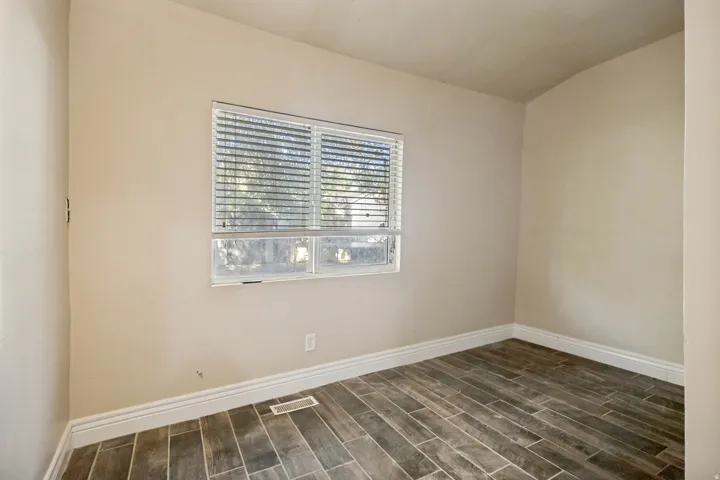 Bright interior room featuring a window with blinds, wood-finish flooring, and white baseboards