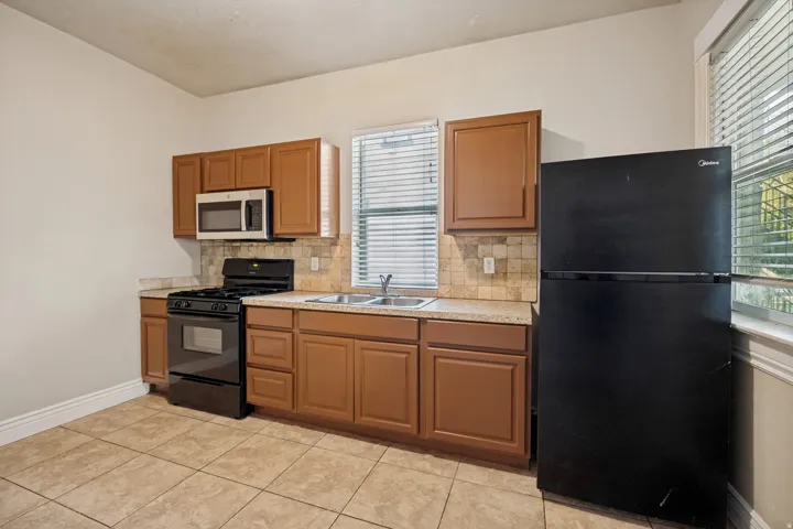 Kitchen featuring wood-finish cabinetry, tile flooring, stone-look countertops, and a tile backsplash