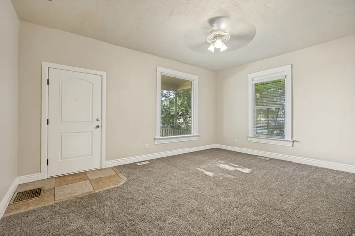 Entry room featuring light beige wall paint, two large windows with blinds, a white paneled entry door, and a ceiling fan with light fixture