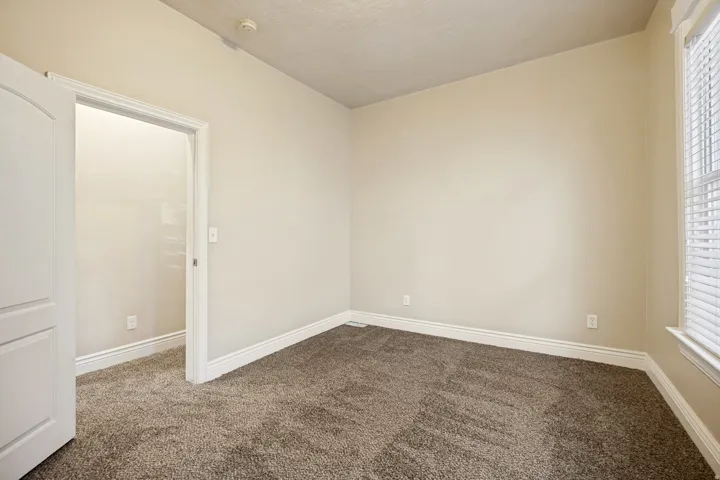 Neutral tone wall paint with white trim, textured carpet, window with blinds, and an arched interior doorway