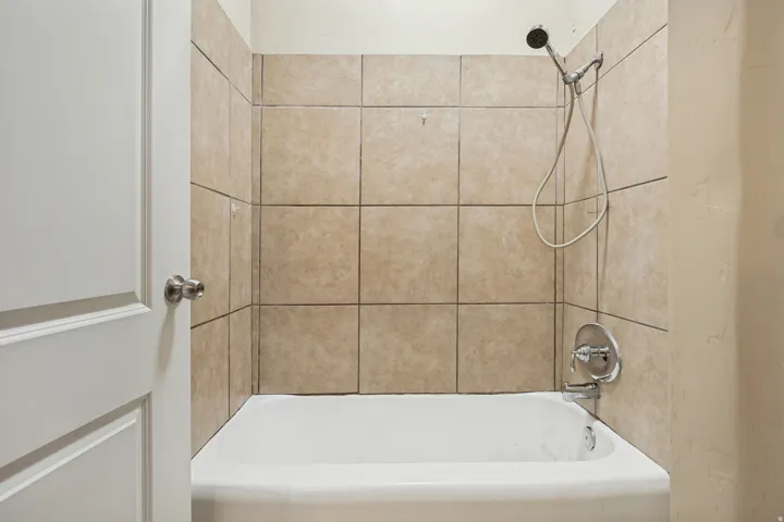 White bathtub with a neutral-toned tile surround and chrome fixtures