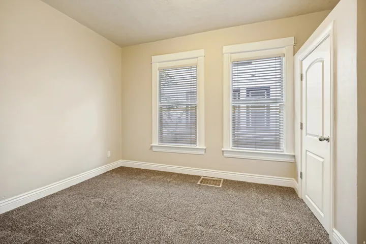 Carpeted room with two windows featuring blinds, neutral paint, white trim, and a white paneled door