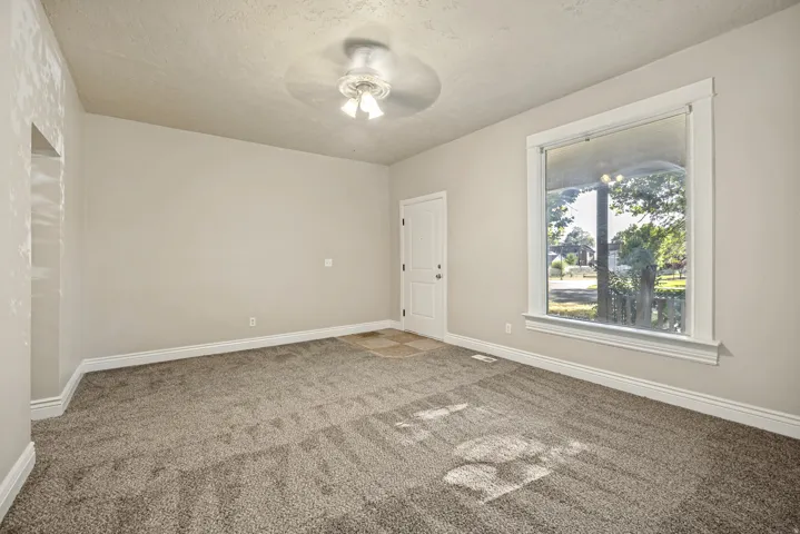 Spacious room featuring neutral paint, plush carpeting, a large window with white trim, and a ceiling fan light fixture