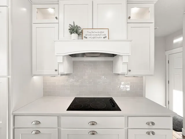 White shaker-style cabinetry with cup pull hardware, built-in electric cooktop, light-toned countertop, and subway tile backsplash