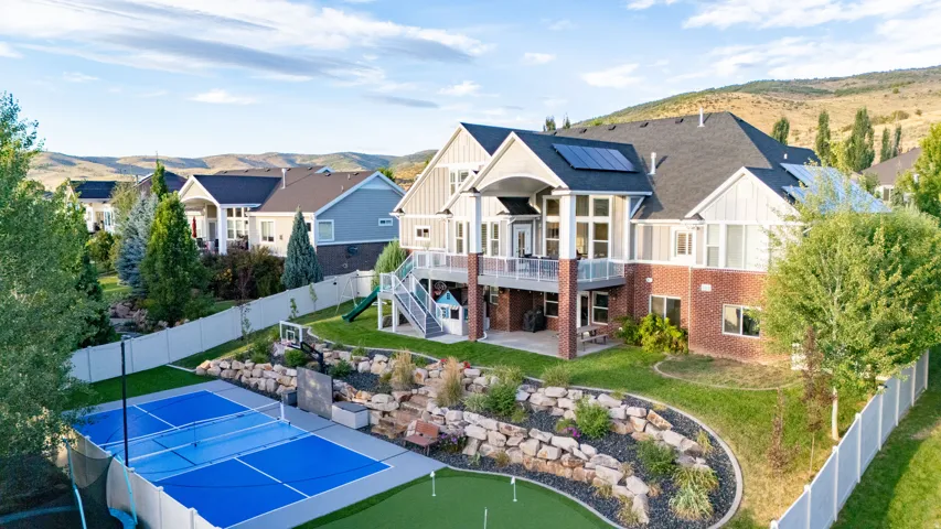 Two-story home with brick and siding exterior, upper-level balcony, ground-level patio, and solar panels