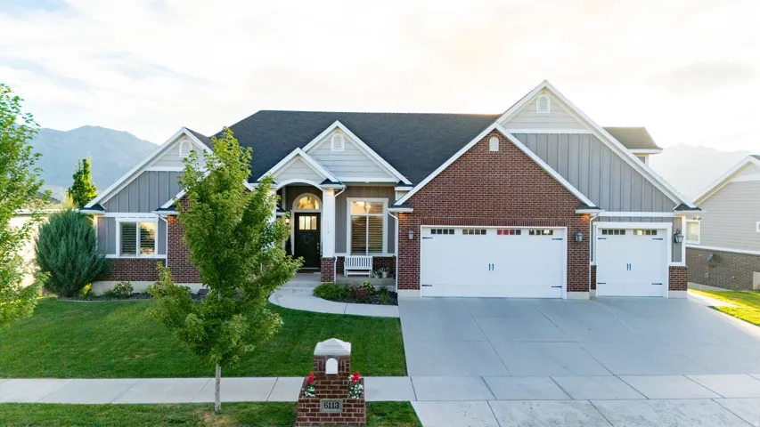 Brick and siding exterior, arched entry, multiple garage bays, concrete driveway, and manicured landscaping