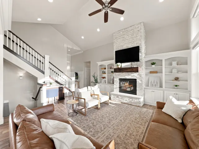 Vaulted ceilings with recessed lighting, stone-finish fireplace with wood mantel, built-in shelving and cabinetry, wood-finish flooring, and a ceiling fan
