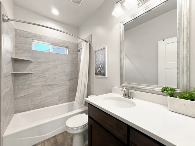 Bathroom featuring a shower/tub combination with gray tile surround, built-in shower shelves, wood-finish flooring, and a vanity with a white countertop