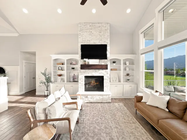 Vaulted ceilings featuring recessed lighting, a stone-clad fireplace with a wood mantle, built-in shelving, wood-finish flooring, and expansive windows