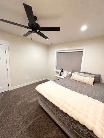 Recessed lighting, ceiling fan with integrated lighting, window with roller shade, white trim, and dark carpeting
