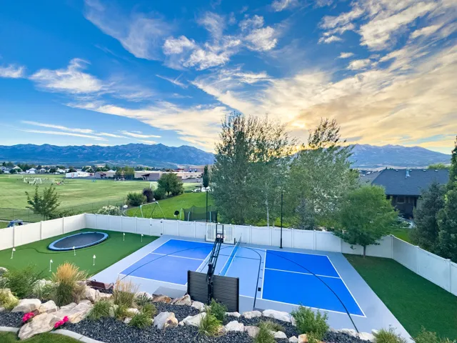Sport court with blue and gray surfacing, integrated basketball hoop, and surrounding green turf