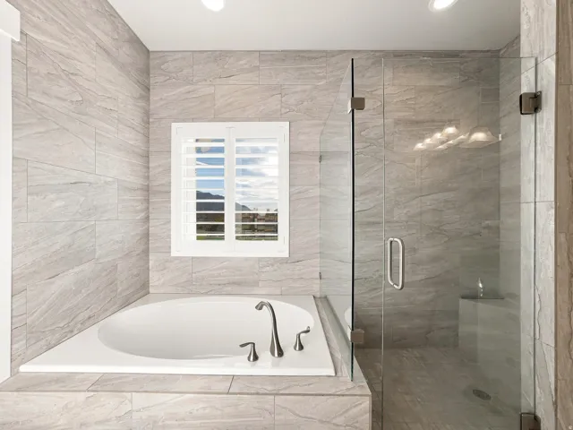 Built-in soaking tub with brushed nickel fixtures, custom plantation shutters, and a glass-enclosed shower with a built-in bench