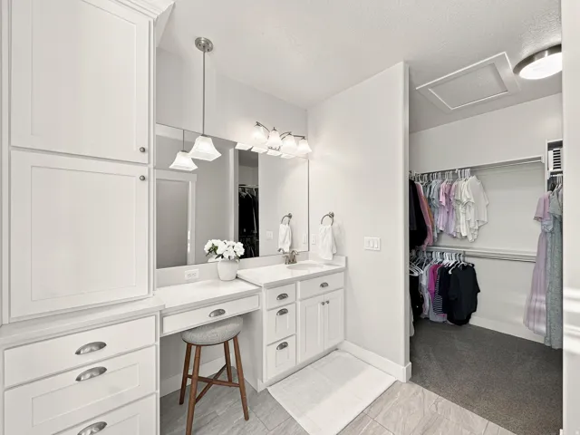 Built-in cabinetry with ample storage, vanity counter with integrated sink, walk-in closet with hanging rods, and tiled flooring