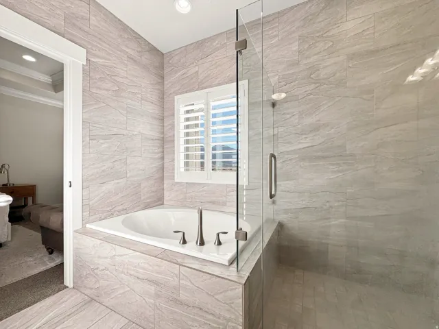 Built-in soaking tub with deck-mounted fixtures, separate glass-enclosed shower, and plantation shutters