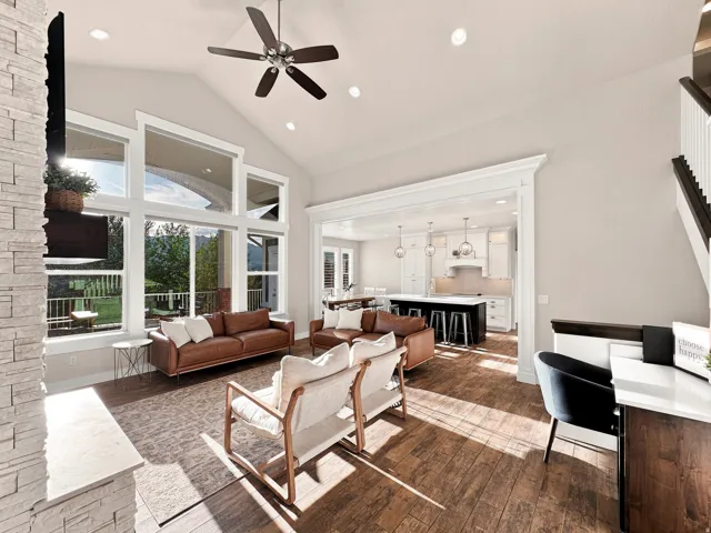Vaulted ceiling with recessed lighting, large picture windows, wood-finish flooring, stone-clad fireplace, and a decorative archway