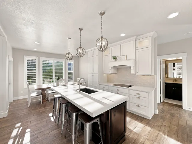 Gourmet kitchen with white cabinetry, stainless steel sink, large kitchen island with seating, wood-finish flooring, and pendant lighting