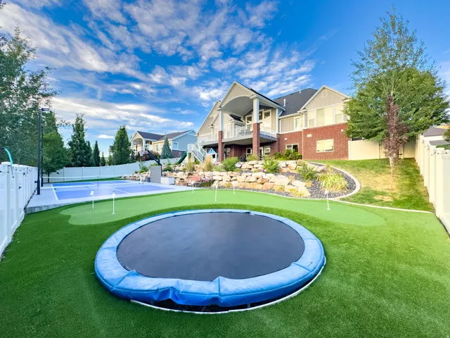 Expansive backyard featuring artificial turf, a putting green, and a multi-sport court