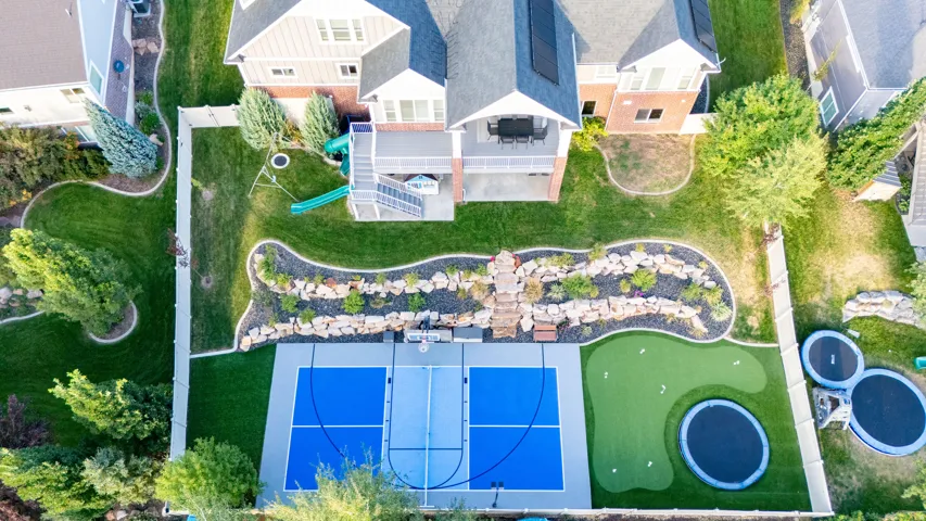 Expansive backyard featuring a multi-sport court, artificial turf putting green, and landscaped rock garden