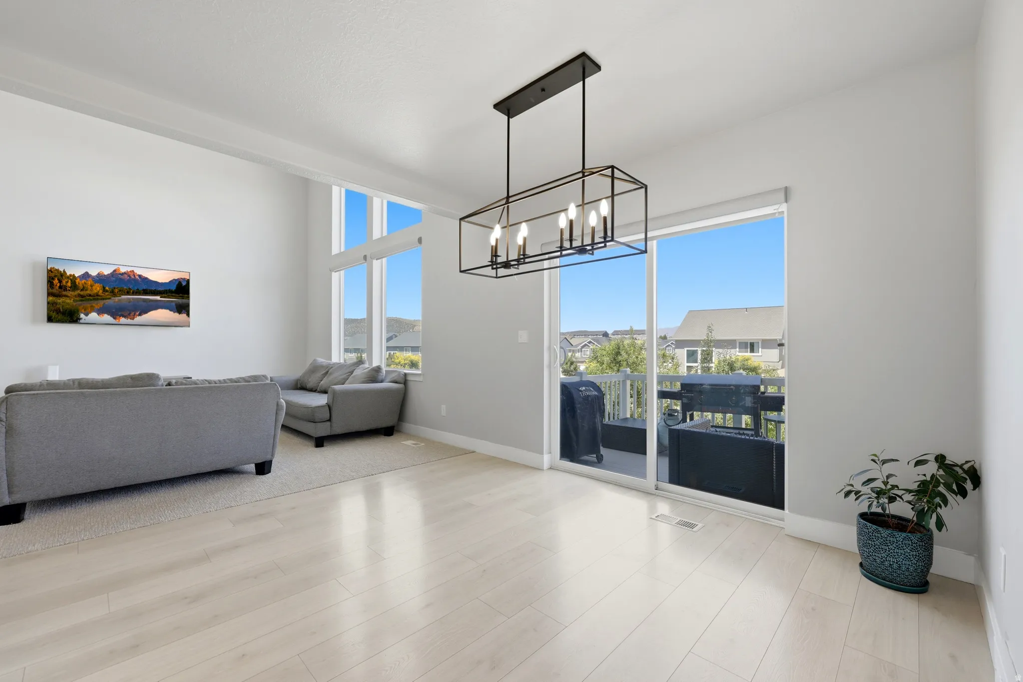Open-concept living space featuring high ceilings, wood-finish flooring, a modern linear chandelier, and expansive windows