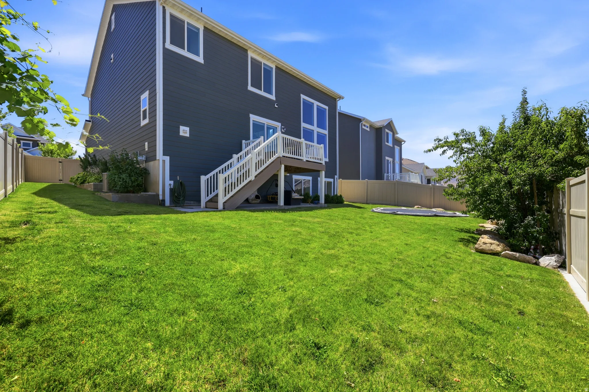 Spacious backyard featuring a manicured lawn, full privacy fencing, and a multi-level deck with white railings
