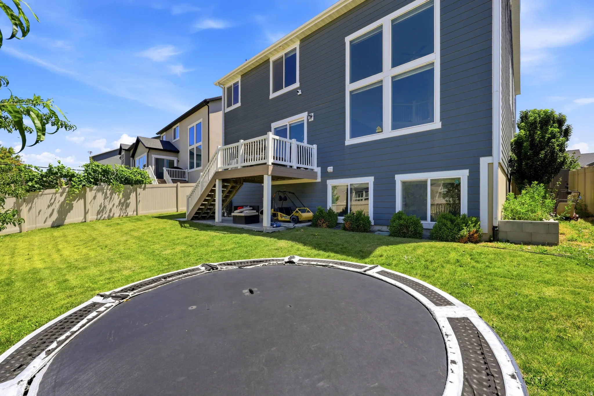 Expansive backyard featuring a manicured lawn, a two-story residence with gray siding, and an upper-level deck with white railings