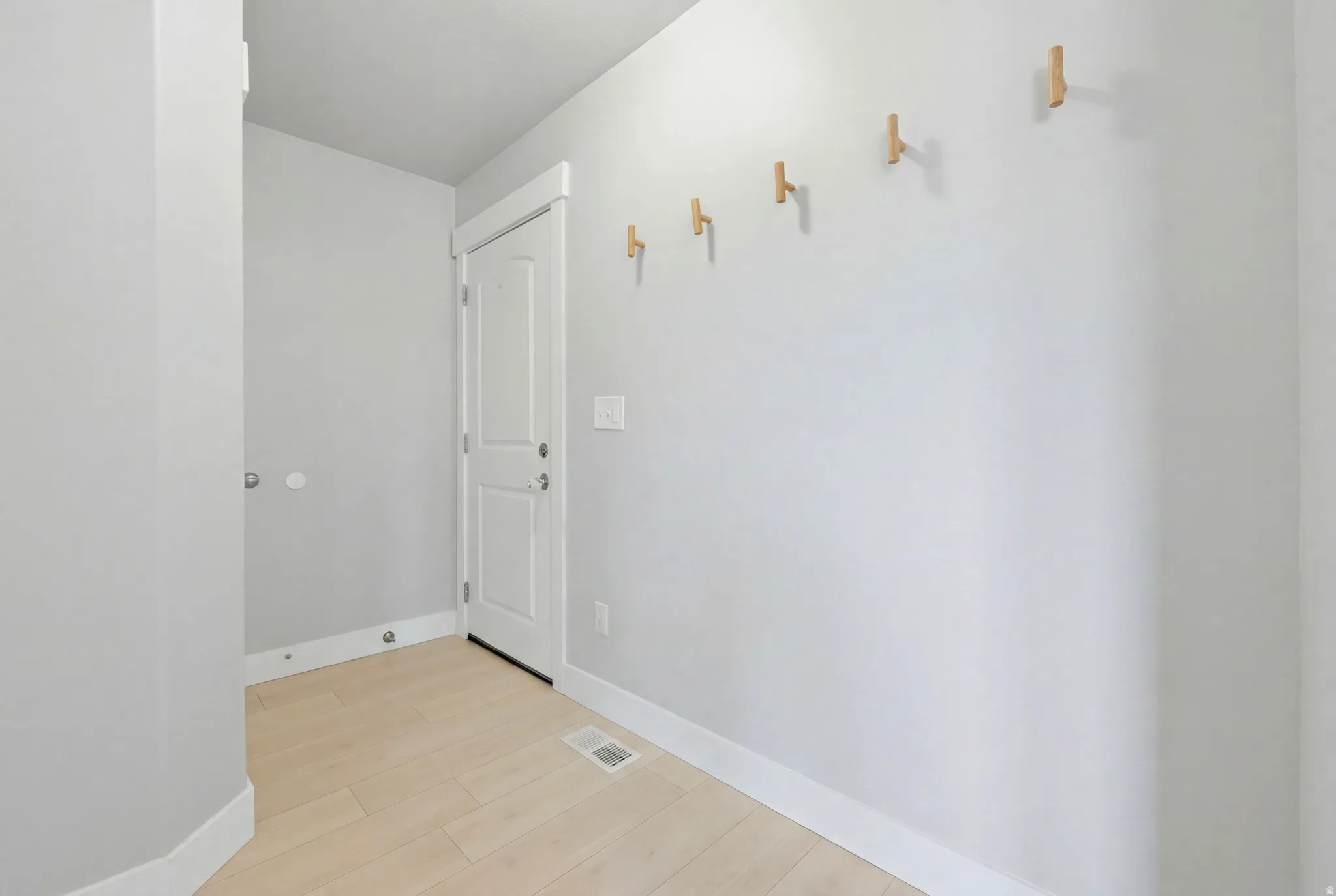 Entryway featuring light-toned wood-finish flooring, a white paneled door, and a row of five wooden wall hooks