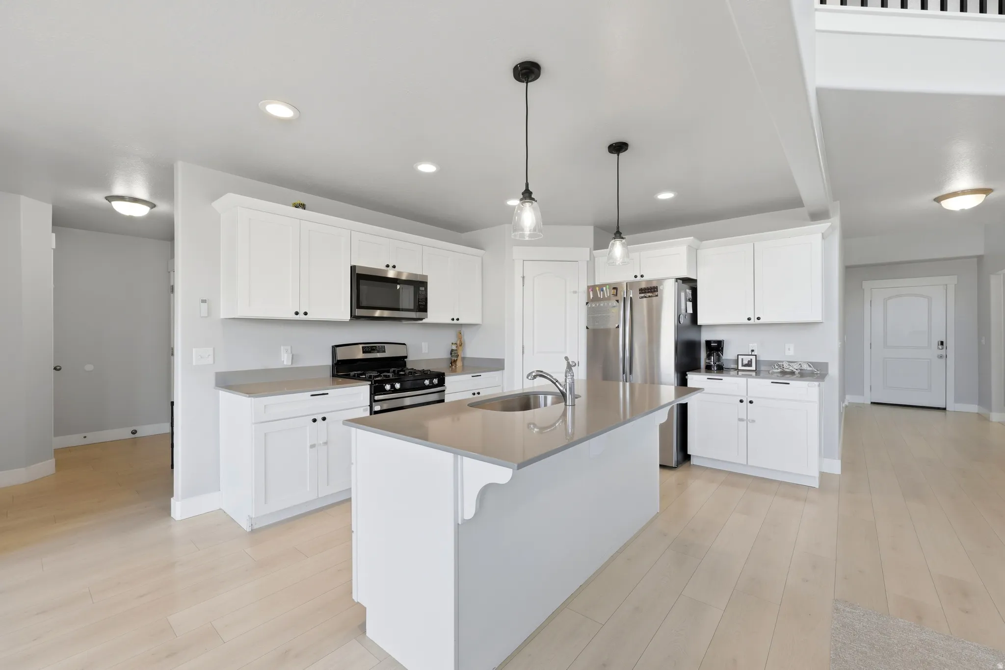 Open-concept kitchen featuring an island with an undermount sink, stainless steel appliances, white cabinetry, and light wood-finish flooring