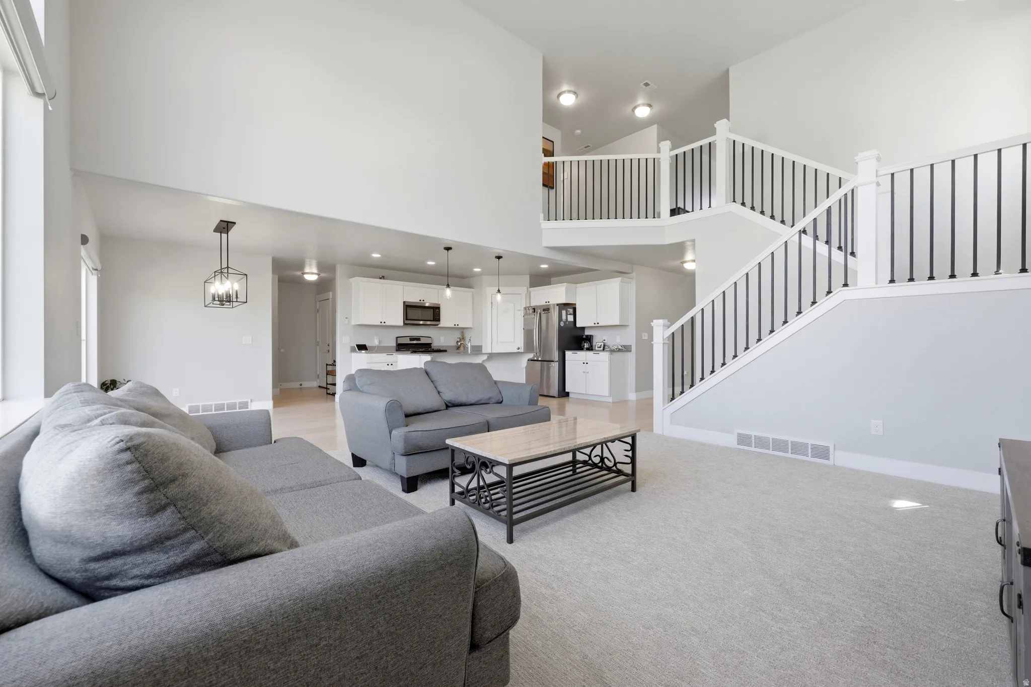 Spacious living area featuring a two-story ceiling, light gray carpet, and a white and black staircase with black iron spindles