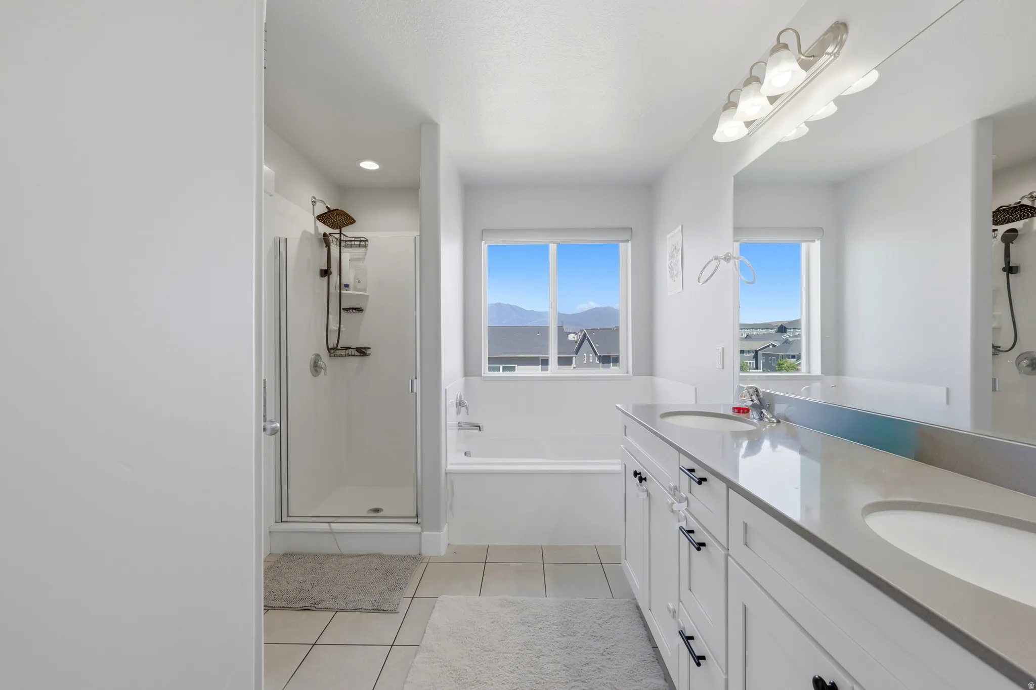 Bright bathroom featuring a double vanity with stone countertops, an integrated soaking tub, and a separate glass-enclosed shower