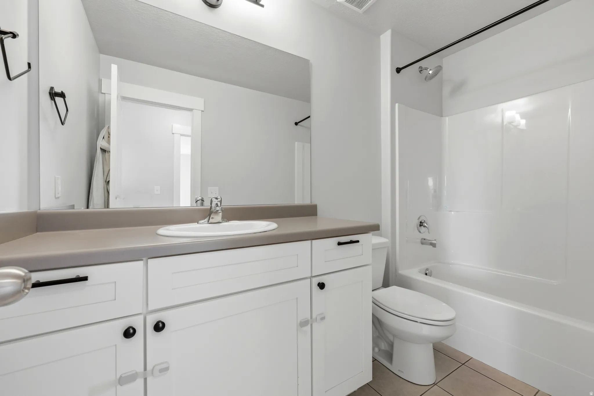 Bathroom featuring a white vanity with a single basin sink, a neutral countertop, and a white tub/shower combination with a black shower curtain rod