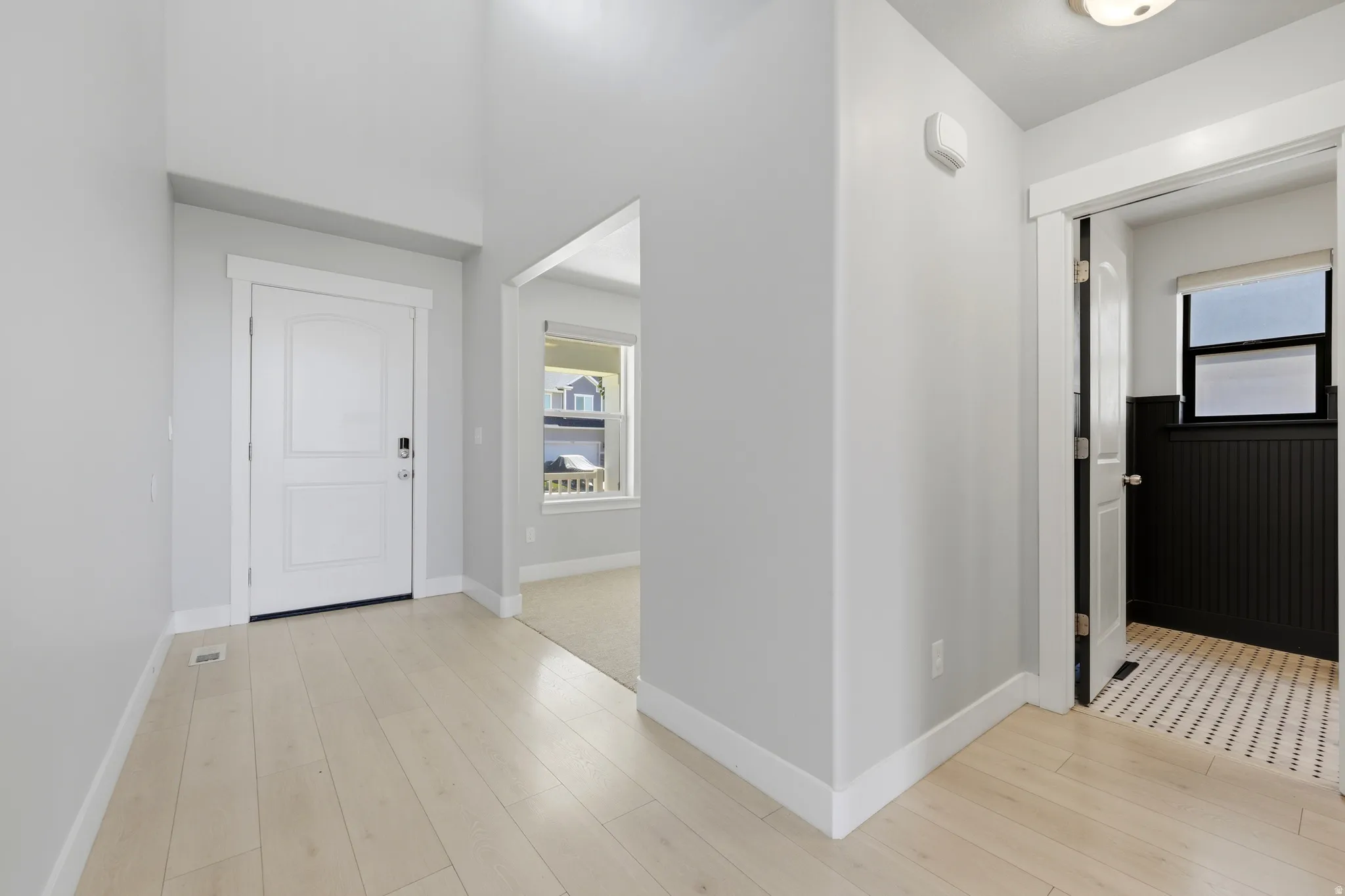 Bright entryway featuring light wood-finish flooring, a white paneled door with smart lock, and tall ceilings
