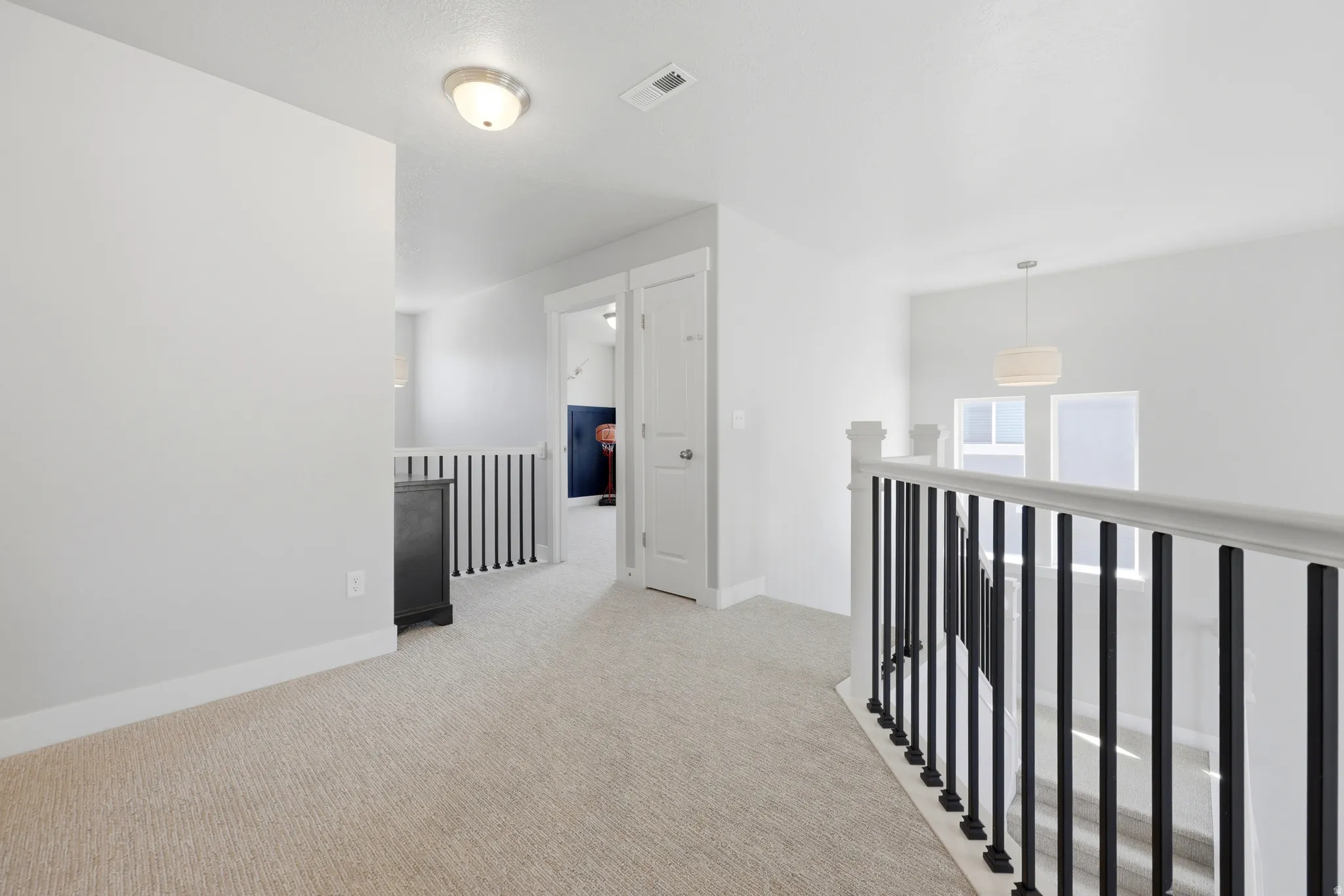 Carpeted upper-level landing featuring a white painted railing with black spindles and white walls