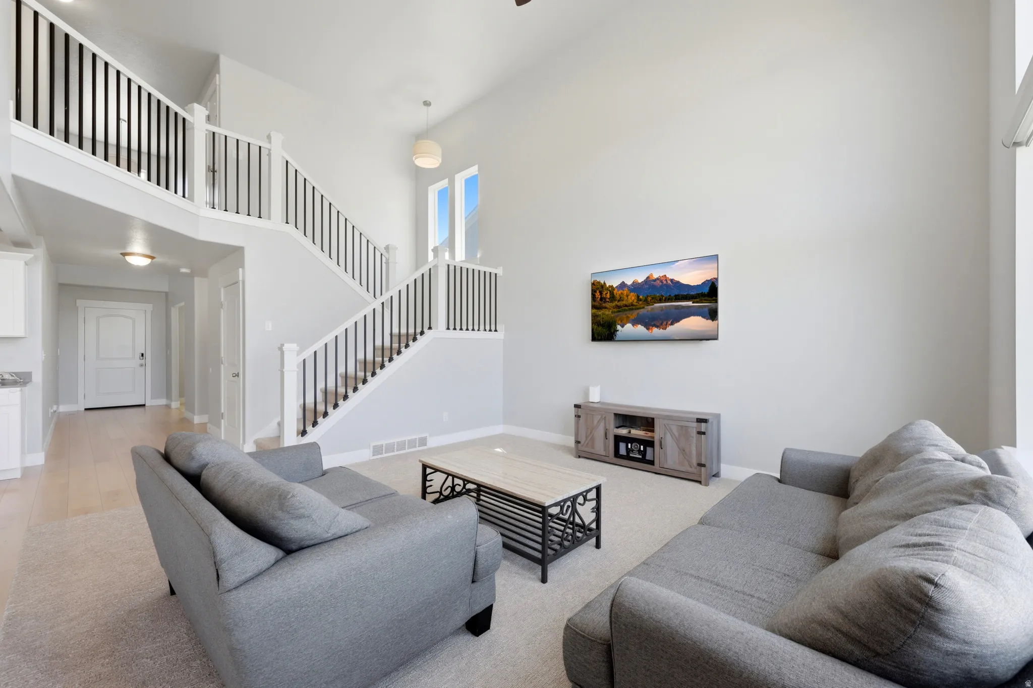 Spacious living area featuring high vaulted ceilings, light-colored carpeting, and large windows providing ample natural light