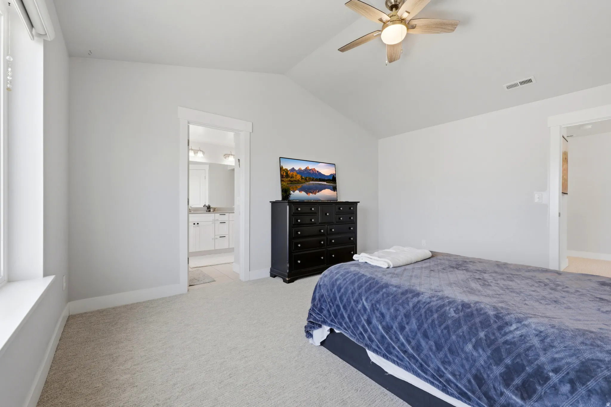 Carpeted room with a vaulted ceiling, a ceiling fan with integrated lighting, and a white-trimmed window