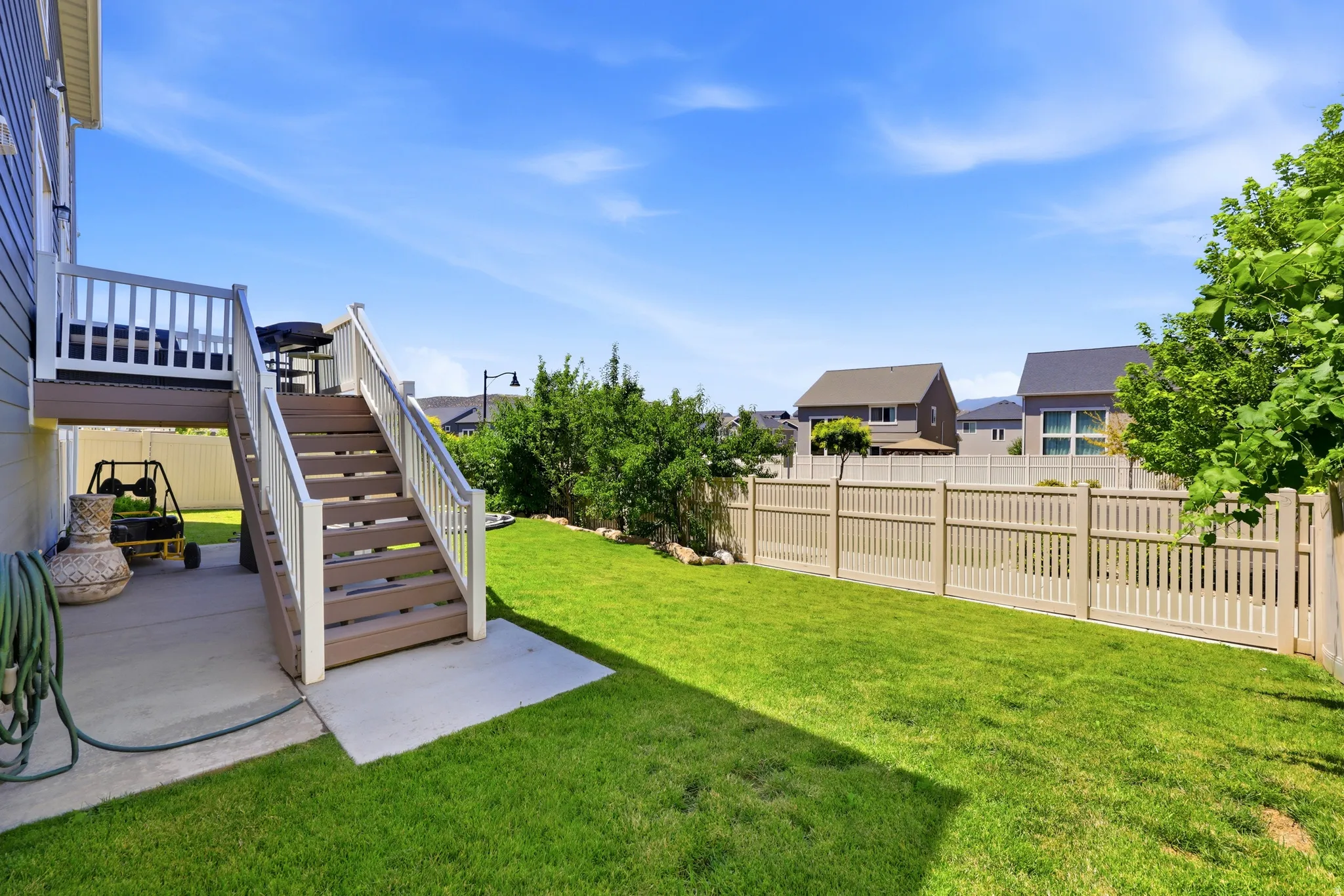 Backyard featuring a green lawn, durable fencing, and a multi-level deck with stairs to a lower concrete patio