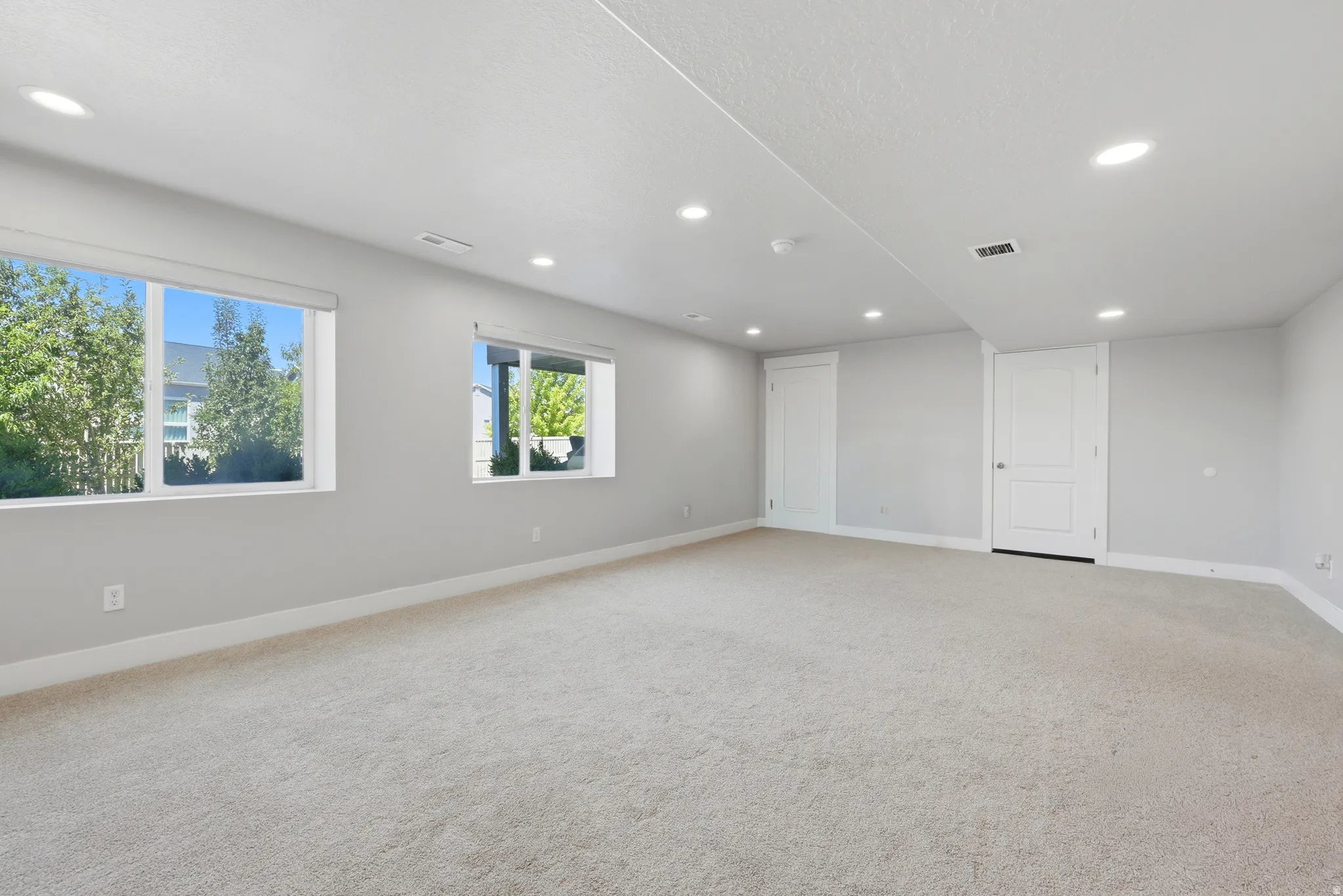 Spacious room featuring neutral carpet, recessed lighting, two windows with white trim, light gray walls, and two white paneled doors