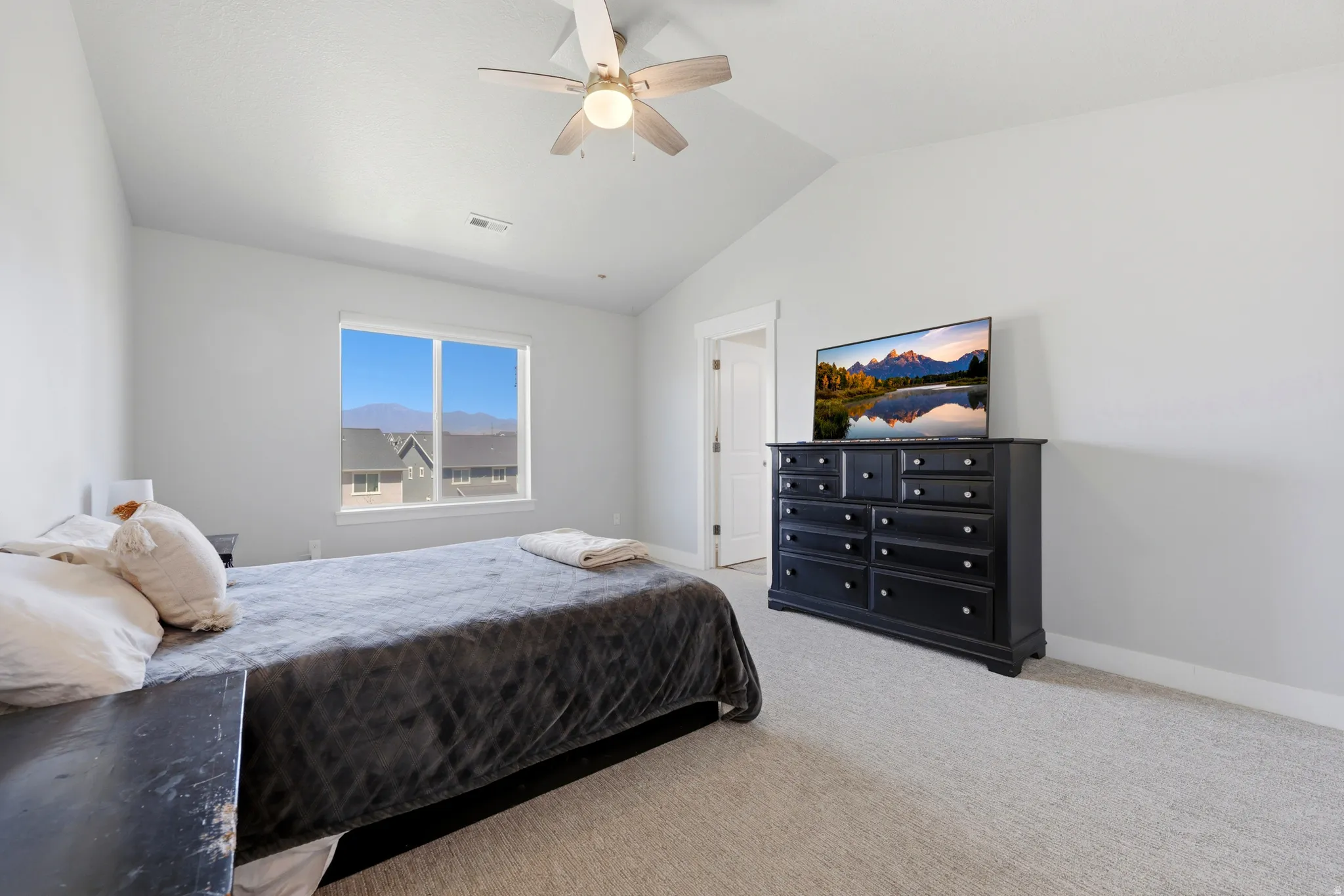Carpeted bedroom featuring a vaulted ceiling with a ceiling fan, a window overlooking distant mountains, and light-colored walls
