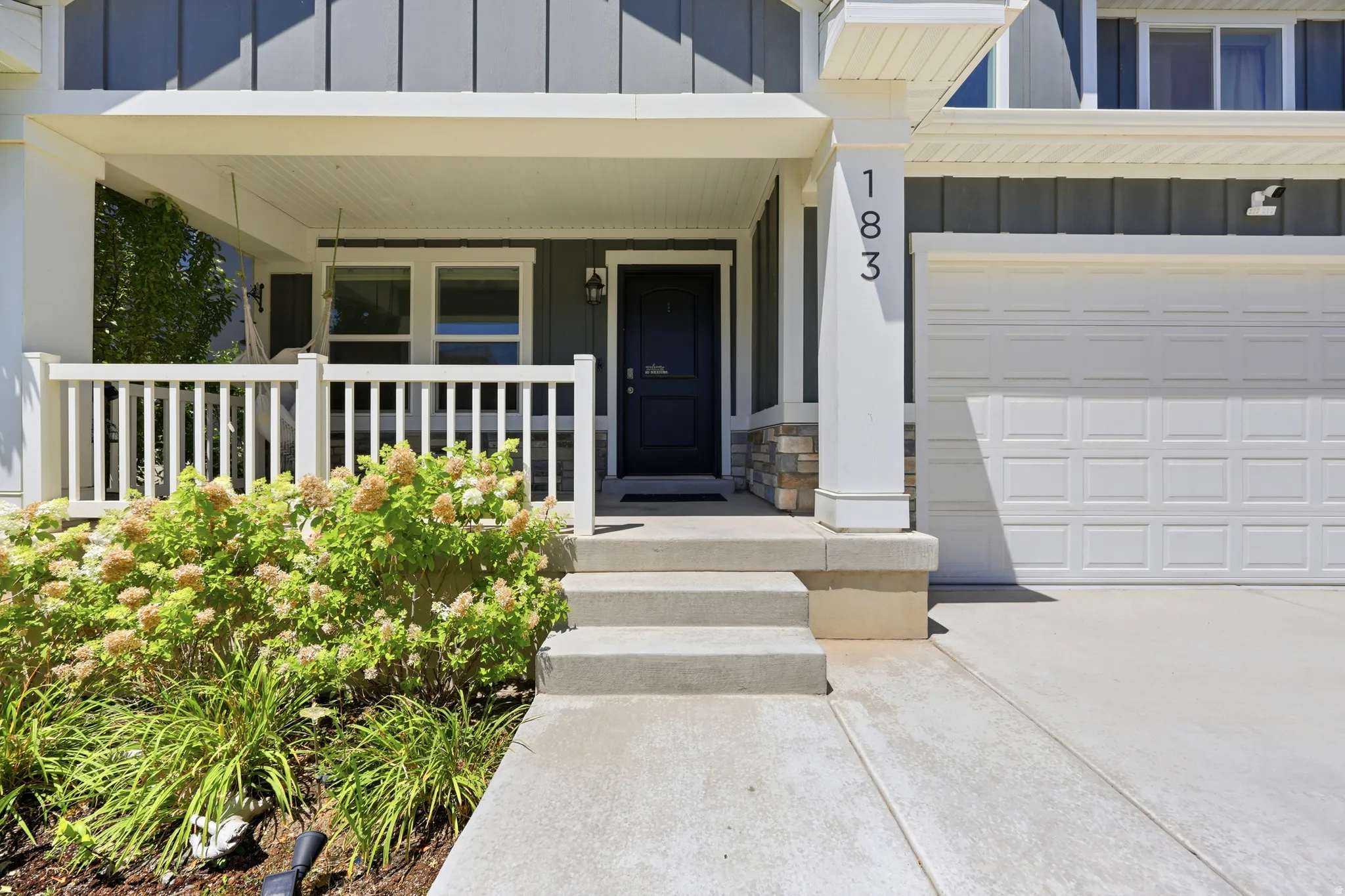 Covered front porch with white railings, stone pillar accents, and a dark entry door