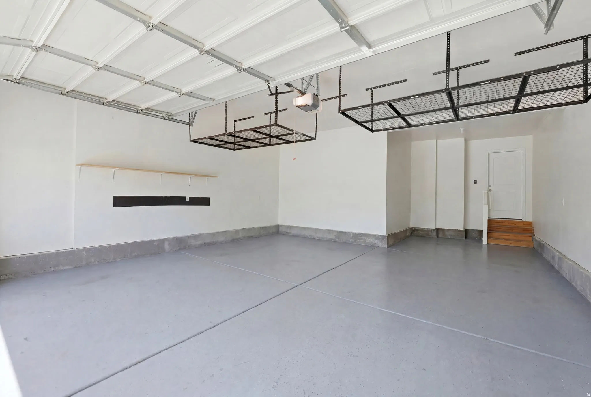 Spacious garage featuring a durable epoxy-coated concrete floor, overhead storage racks, a utility shelf, a rear access door, and a paneled garage door