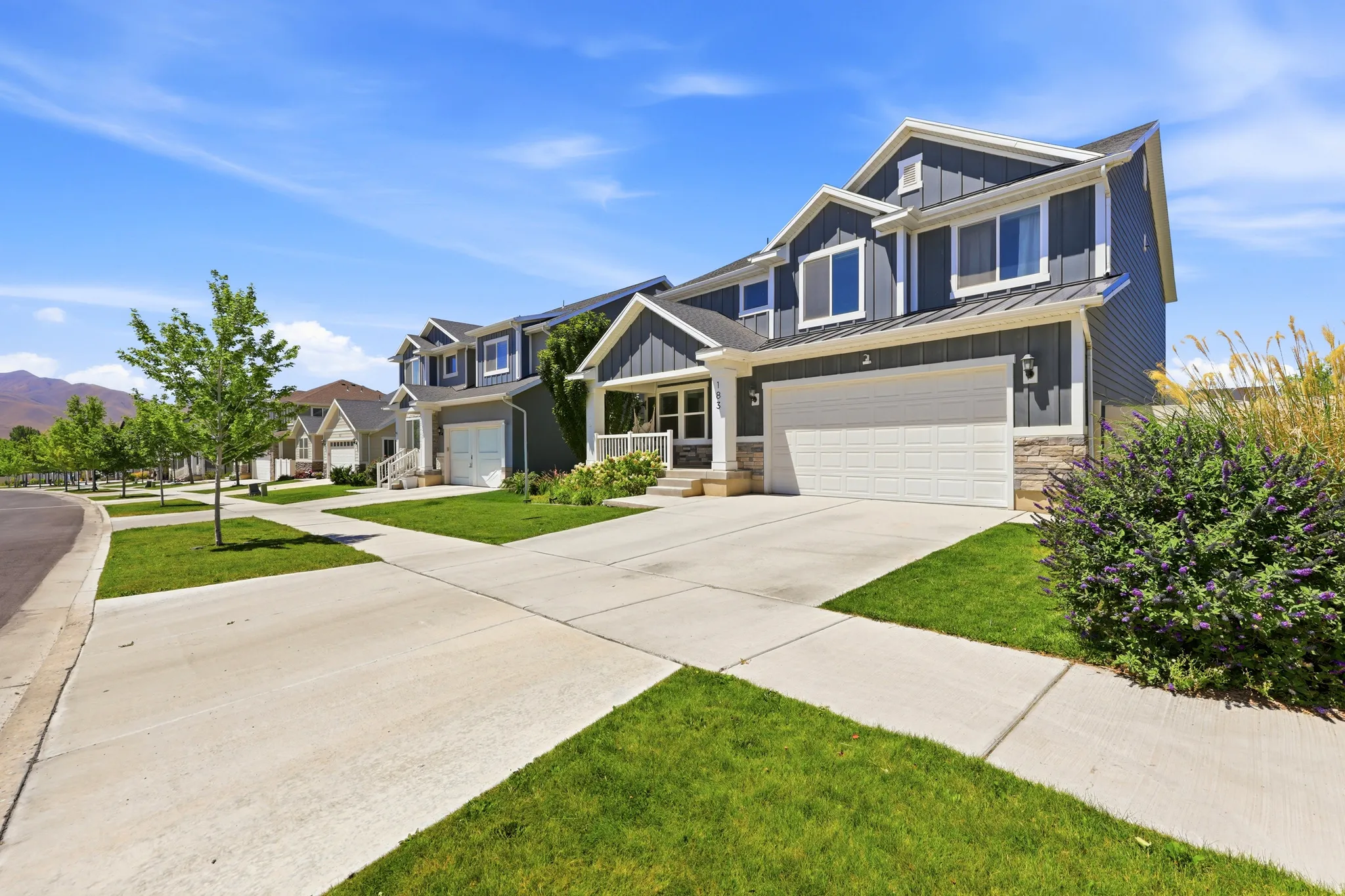 Contemporary residence featuring a two-car garage, gray vertical siding, stone accents, and a covered porch with white columns