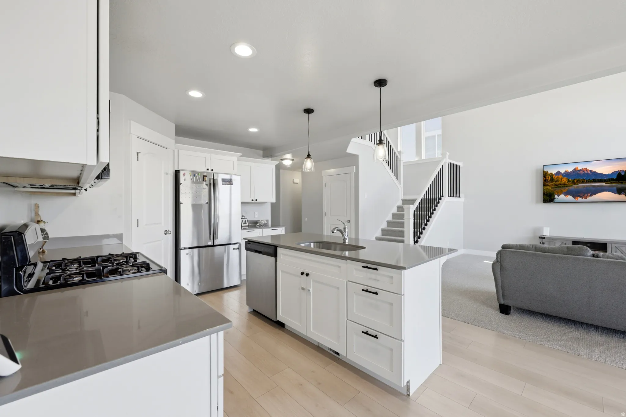 Contemporary kitchen featuring a gas range, stainless steel appliances, and a central island with a sink and pendant lighting
