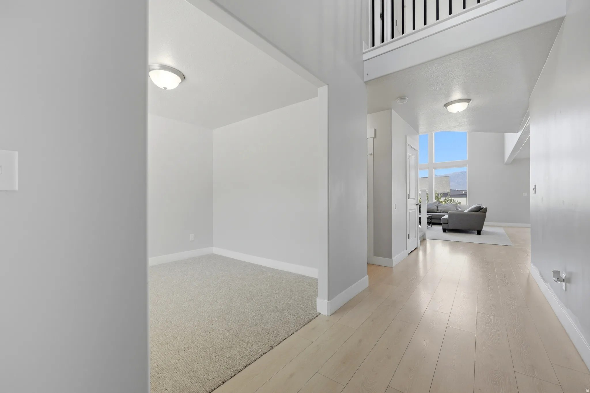 Light-toned wood-finish flooring extending into an open living area with large windows, complemented by a carpeted recessed space