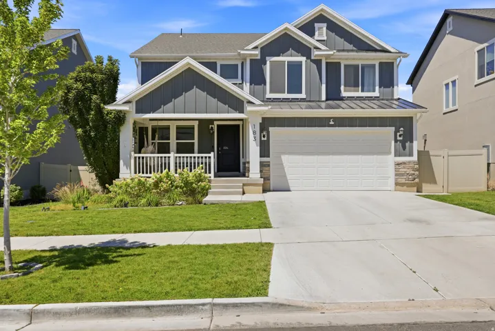 Contemporary two-story residence featuring a dark gray vertical siding facade, a covered front porch with white railings, a two-car garage with a white door, stone accents, and a concrete driveway