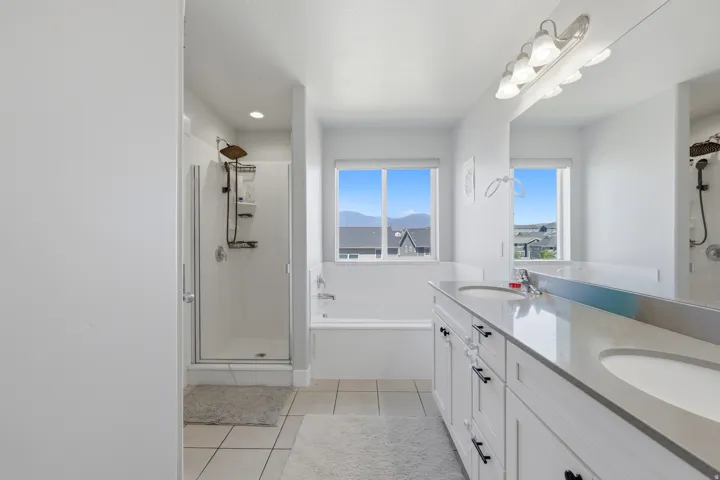Bright bathroom featuring a double vanity with stone countertops, an integrated soaking tub, and a separate glass-enclosed shower
