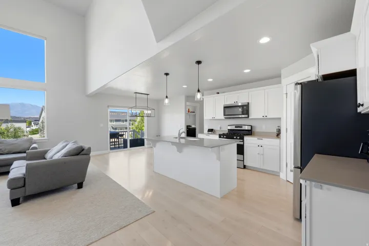 Open-concept living area featuring a two-story ceiling, large windows, light wood-finish flooring, and a contemporary kitchen with white cabinetry and an island
