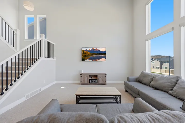 Two-story living area featuring a prominent staircase with black metal balusters and white risers, expansive two-story windows with roller shades, and light-colored carpeting