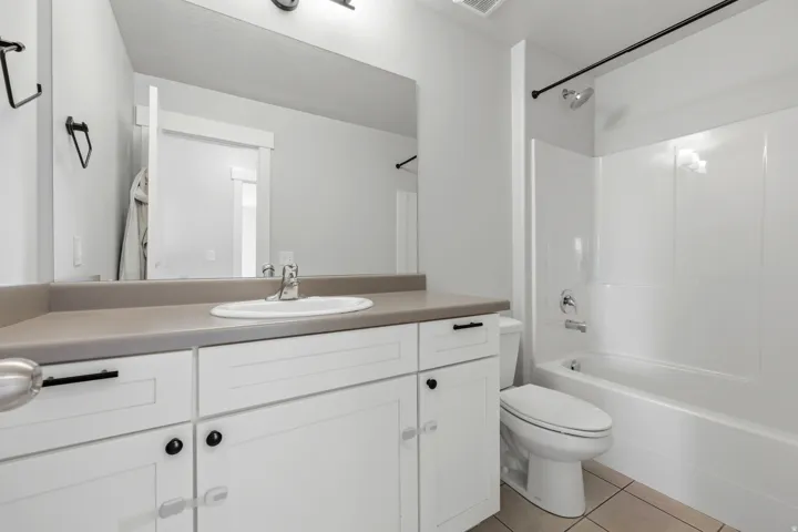 Bathroom featuring a white vanity with a single basin sink, a neutral countertop, and a white tub/shower combination with a black shower curtain rod
