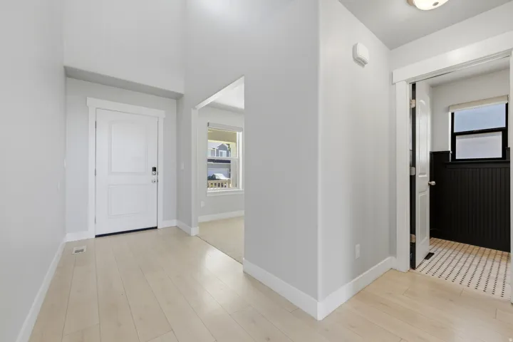 Bright entryway featuring light wood-finish flooring, a white paneled door with smart lock, and tall ceilings