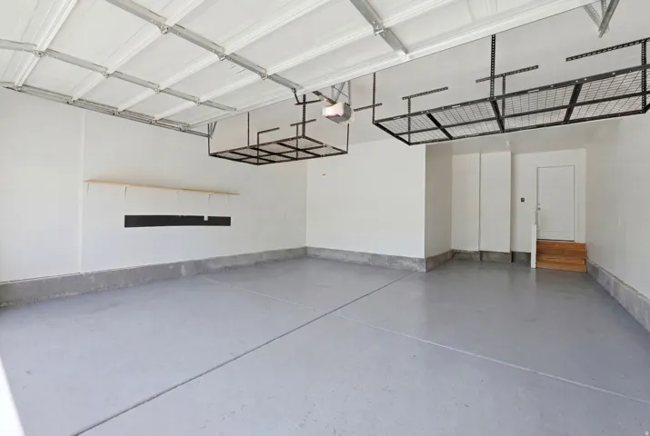 Spacious garage featuring a durable epoxy-coated concrete floor, overhead storage racks, a utility shelf, a rear access door, and a paneled garage door