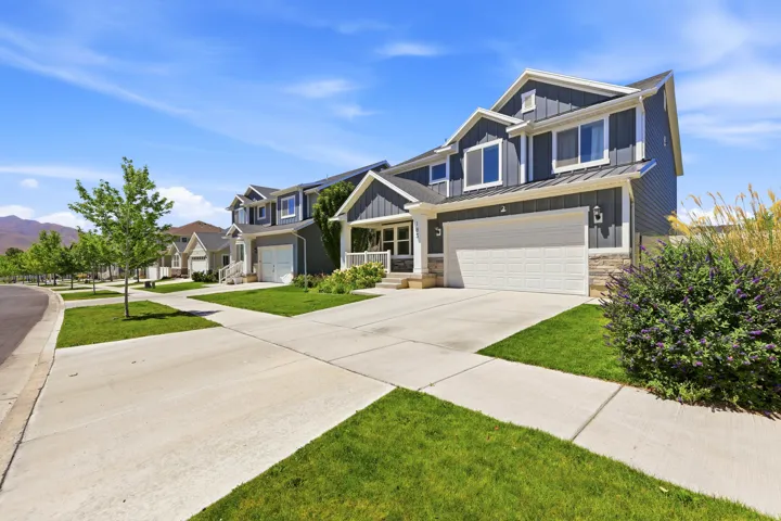 Contemporary residence featuring a two-car garage, gray vertical siding, stone accents, and a covered porch with white columns